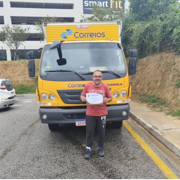 Motorista de veículo de carga exibe certificado de formação ao lado do caminhão
